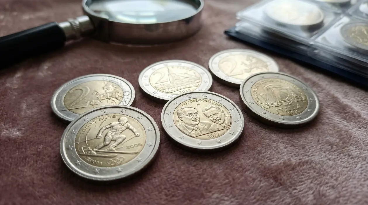 Monete da due euro commemorative disposte su un panno vicino a una lente di ingrandimento
