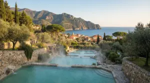 Piscine termali immerse nel verde con vista su un borgo costiero e montagne in lontananza