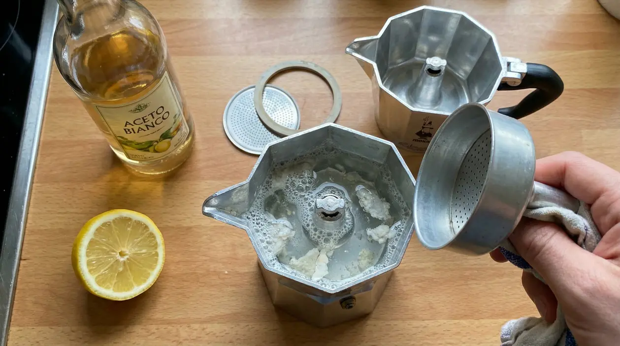 Moka smontata con incrostazioni di calcare, aceto bianco e mezzo limone su un piano cucina